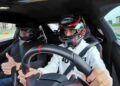 Two people wearing helmets are seated in a car, with one driving and the other giving a thumbs-up—much like what two-time MotoGP champ Francesco Bagnaia might do after experiencing the Lamborghini Temerario.