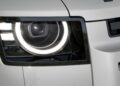Close-up of the Land Rover Defender Refreshed: Here's What’s New For 2026, showcasing its modern left headlight with a circular LED daytime running light and surrounding bodywork in a light color.