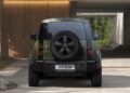 Rear view of a green Land Rover Defender Refreshed: Here's What’s New For 2026, parked on a concrete driveway in front of a modern wooden garage door.