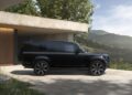 A black Land Rover Defender Refreshed is parked on a concrete driveway outside a modern house, with a scenic view of hills and trees in the background—showing what’s new for 2026.