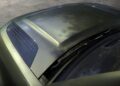 Close-up view of the hood and windshield of a green Land Rover Defender Refreshed: Here's What’s New For 2026, highlighting air vents and reflecting trees and sky on the glossy surface.