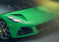 Close-up of the front of a green Lotus Emira with sleek headlights, large alloy wheels, and a blurred yellow light effect highlights the sporty design of this Lotus flagship.