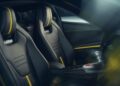 Two black sports car seats with yellow accents and "Lotus" branding, viewed from the passenger side of the 2026 Emira V6. The interior features a manual gear shifter and a minimalistic design, embodying true Lotus Emira style.