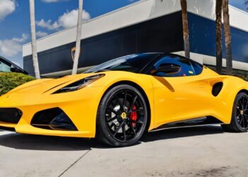 A yellow sports car with black wheels, for sale as the best sports car under $100k, is parked outside a modern building with palm trees in the background.