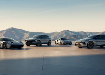 Four modern silver sports cars are parked side by side on a flat surface with mountains and a clear sky in the background.