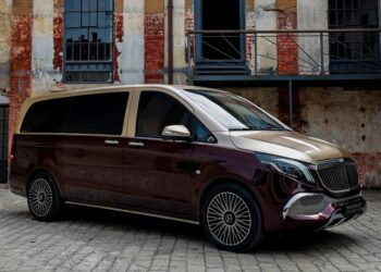 A luxury minivan with a two-tone maroon and gold exterior—a unique creation—is parked on cobblestone in front of a weathered brick building.