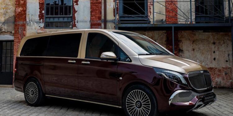 A luxury minivan with a two-tone maroon and gold exterior—a unique creation—is parked on cobblestone in front of a weathered brick building.