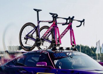 Two purple Canyon Aeroad Road Bikes are mounted on the roof rack of a parked Mercedes-AMG sports car at an outdoor event.