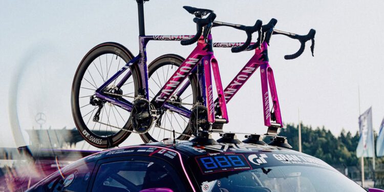 Two purple Canyon Aeroad Road Bikes are mounted on the roof rack of a parked Mercedes-AMG sports car at an outdoor event.