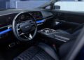The 2026 Optiq-V Cadillac boasts a modern car interior featuring a digital dashboard, multifunction steering wheel, quilted leather seats, and a center console with rotary controls and cup holders.