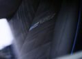 Close-up of a 2026 Optiq-V car seat featuring perforated black leather upholstery, blue stitching, and an embroidered V logo on the backrest—a signature Cadillac design with 519HP performance.