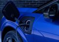 A close-up of a blue 2026 Cadillac Optiq-V electric vehicle being charged, with the cable plugged into the port—showcasing its impressive 519HP.