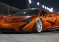 A metallic orange sports car with sleek aerodynamic design and silver alloy wheels is parked on a paved surface at night under bright lights, reminiscent of the 20 Ultra-Exclusive 1-of-1 McLarens being offered in a historic sale.