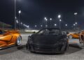 Three luxury sports cars, including two orange and one black, are parked on a well-lit racetrack at night under stadium lights—evoking the allure of the 20 Ultra-Exclusive 1-of-1 McLarens being offered in a historic sale.