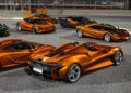 A group of orange McLaren sports cars, including 20 ultra-exclusive 1-of-1 McLarens being offered in a historic sale, are parked on a racetrack at night, with various models displayed in an outdoor setting.