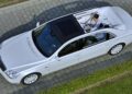 A white Mercedes-Maybach G650 For Sale, this luxury sedan features an open roof and is viewed from above, with two people relaxing in the rear passenger compartment.