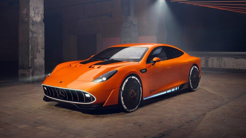 An orange Mercedes-AMG GT XX Concept sports car is parked indoors on a brick floor under focused lighting in an industrial setting.