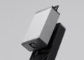 A close-up of a rectangular electronic device from Olto, featuring a small lens, partially removed from a black base, against a plain grey background.