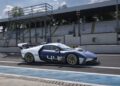 A blue and white Maserati MCXtrema race car with the number 44 drives on a racetrack at Monza near empty grandstands and fencing under a clear sky.