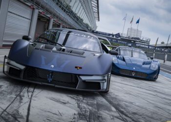 Two blue Maserati MCXtrema sports cars are parked on a Monza racetrack pit lane, with a garage and racetrack facilities visible in the background.