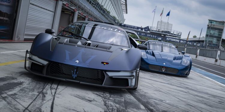 Two blue Maserati MCXtrema sports cars are parked on a Monza racetrack pit lane, with a garage and racetrack facilities visible in the background.