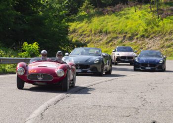 Four Maserati cars, including a vintage red race car reminiscent of the 1000 Miglia and three modern models, drive on a winding road bordered by greenery.