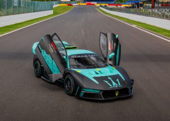 A teal and black Maserati MCXtrema with its butterfly doors open, sporting a Historic Livery, is parked on a race track.