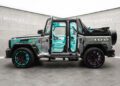 A custom Mansory G-Wagon SUV with graffiti-style paint inspired by Alec Monopoly, open doors, turquoise interior, and mismatched turquoise and purple wheels in a grey showroom.