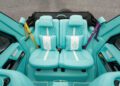 The image shows the interior of a Mansory G-Wagon with two turquoise quilted leather seats, each featuring a cartoon pillow and colored seatbelts, set against sleek gray walls.