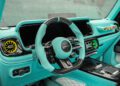Turquoise and black luxury G-Wagon interior featuring a carbon fiber steering wheel, large digital displays, and customized air vents in true Mansory style.