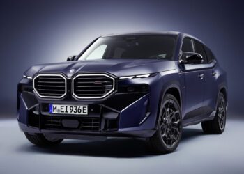 A dark blue 2026 XM Label BMW SUV is shown in a studio setting with dramatic lighting, highlighting its large front grille and modern design details.