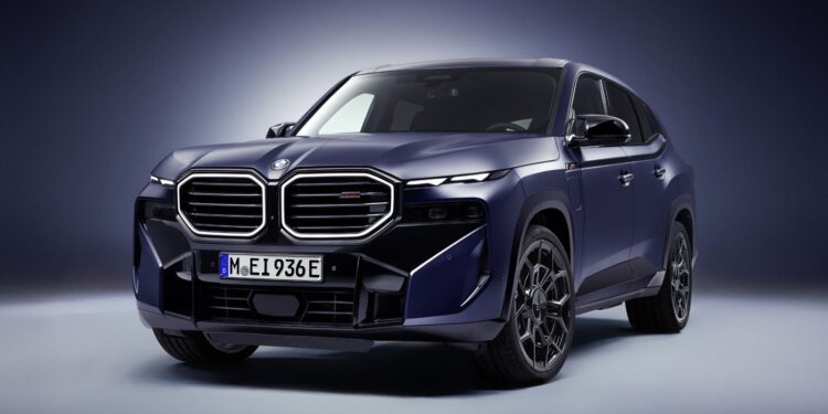 A dark blue 2026 XM Label BMW SUV is shown in a studio setting with dramatic lighting, highlighting its large front grille and modern design details.