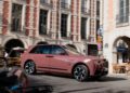 A pink Rolls-Royce Spectre luxury SUV drives through a city street with classic European architecture in the background, capturing the chic elegance of Paris Fashion Week.