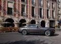 A grey Rolls-Royce Spectre luxury coupe parked on a street in front of a building with arched windows and red brick accents, evoking the elegance of Paris Fashion Week.