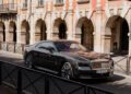 A black Rolls-Royce luxury car is parked on a city street in front of a historical building with arches and red brick accents.