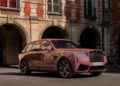 A pink Rolls-Royce SUV is parked in front of an old stone building with arched doorways and balconies, creating a scene worthy of Paris Fashion Week.
