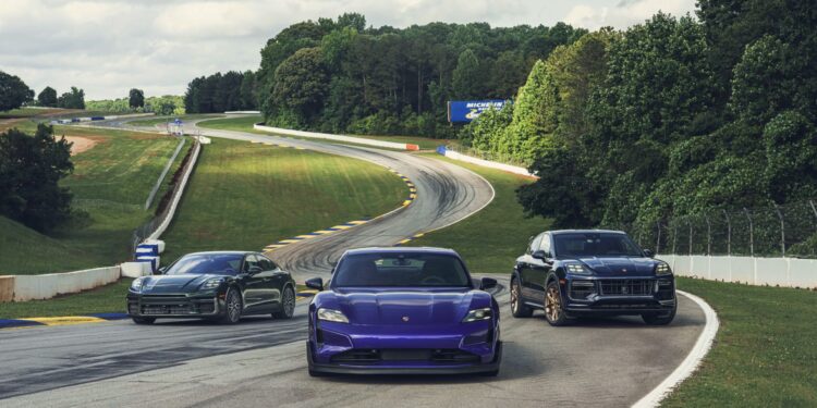 Three Porsche vehicles, including a purple Taycan, are driving on a winding racetrack surrounded by grass and trees.