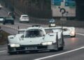 A silver 1-of-1 Porsche 963 RSP Breaks Cover As A Tribute To Penske Ahead Of Le Mans 2025, driving on a public road with other cars and road signs visible in the background.