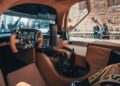 The image shows the tan leather interior and control panel of a modern aircraft or helicopter, with people and a stone building outside—evoking exclusive craftsmanship like the 1-of-1 Porsche 963 RSP Breaks Cover As A Tribute To Penske Ahead Of Le Mans 2025.