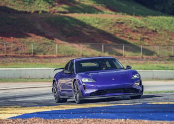A purple Porsche Taycan Turbo GT drives on a racetrack at Road Atlanta, setting its sights on the EV Lap Record amid grass, fencing, and a hillside backdrop.