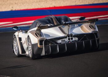 A silver Pagani Huayra R Evo with a large rear wing and distinctive exhaust pipes drives on a racetrack with blue, red, and white curbs, capturing the spirit of the Milano Monza Motor Show.