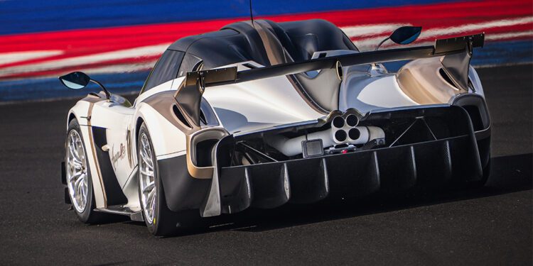 A silver Pagani Huayra R Evo with a large rear wing and distinctive exhaust pipes drives on a racetrack with blue, red, and white curbs, capturing the spirit of the Milano Monza Motor Show.