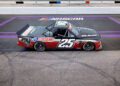 A black and red Ram race truck with a powerful HEMI V8 engine, sporting the number 25, is parked on a NASCAR track near the start/finish line.