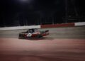 A red and black Ram race truck with the number 25, powered by one of NASCAR’s fierce HEMI V8s, drives on a lit racetrack at night.