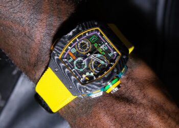 A wrist with a black and yellow high-end sports watch, reminiscent of limited edition watches like the Richard Mille RM65-01, featuring multiple dials and a bright yellow strap.