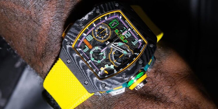 A wrist with a black and yellow high-end sports watch, reminiscent of limited edition watches like the Richard Mille RM65-01, featuring multiple dials and a bright yellow strap.
