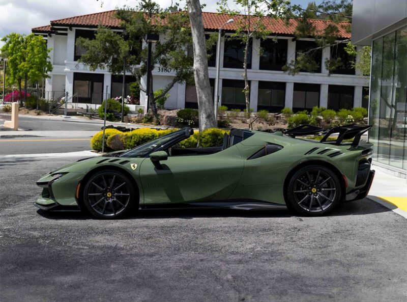 A stunning matte Verde Oliva SF90XX Spider Ferrari convertible is parked on the street in front of a modern white building, surrounded by trees and greenery, showcasing the elegance of Ferrari Westlake.
