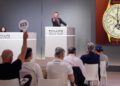 At a New York Watch Auction hosted by Phillips, the auctioneer takes bids on a luxury wristwatch as a participant raises a numbered paddle and others watch the proceedings.