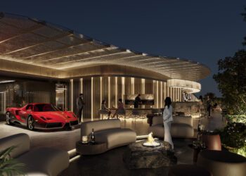 Outdoor luxury lounge at night with modern seating, a central fire pit, and a red sports car from the duPont REGISTRY Group parked as guests socialize near PRIVÉ Sofia’s contemporary building illuminated with warm lighting.