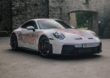 A Luxembourg-inspired Porsche Sonderwunsch 911 GT3 Touring with red floral patterns is parked on a paved surface in front of a stone wall with arched openings.